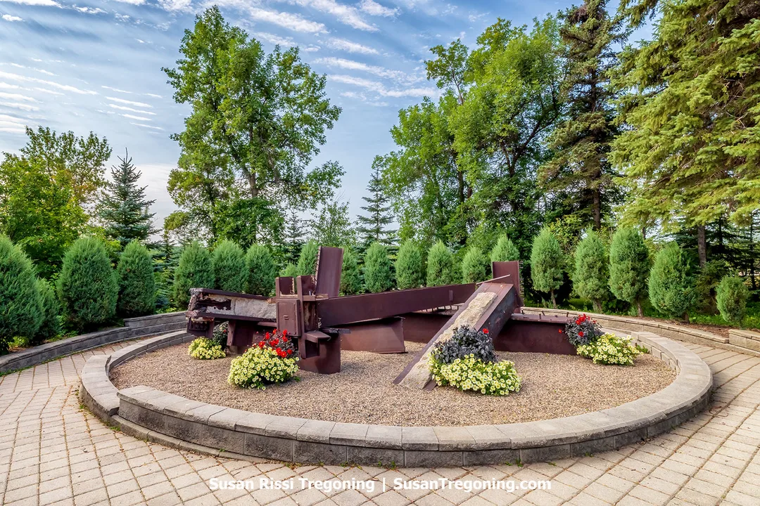 A circular memorial garden at the International Peace Garden featuring rusted steel beams recovered from the World Trade Center, surrounded by flowers and trees to honor the victims of September 11, 2001.