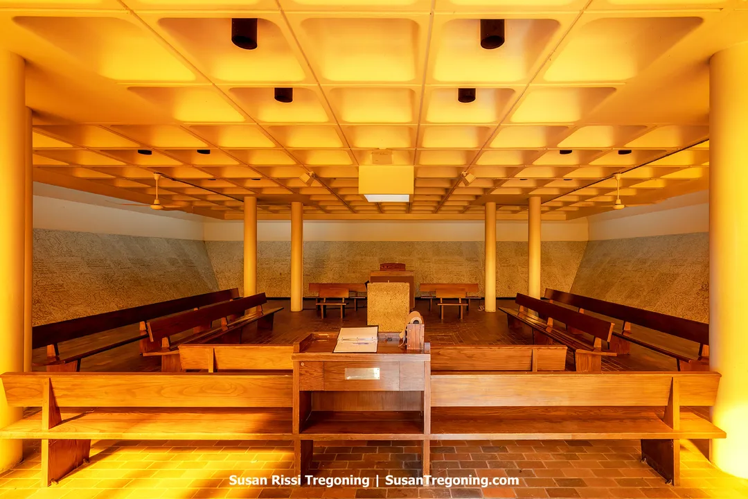 Interior of the Peace Chapel at the International Peace Garden, built in 1968, with Manitoba limestone walls carved with quotations on peace and warm golden light filtering through French-colored glass, creating a quiet, contemplative atmosphere.