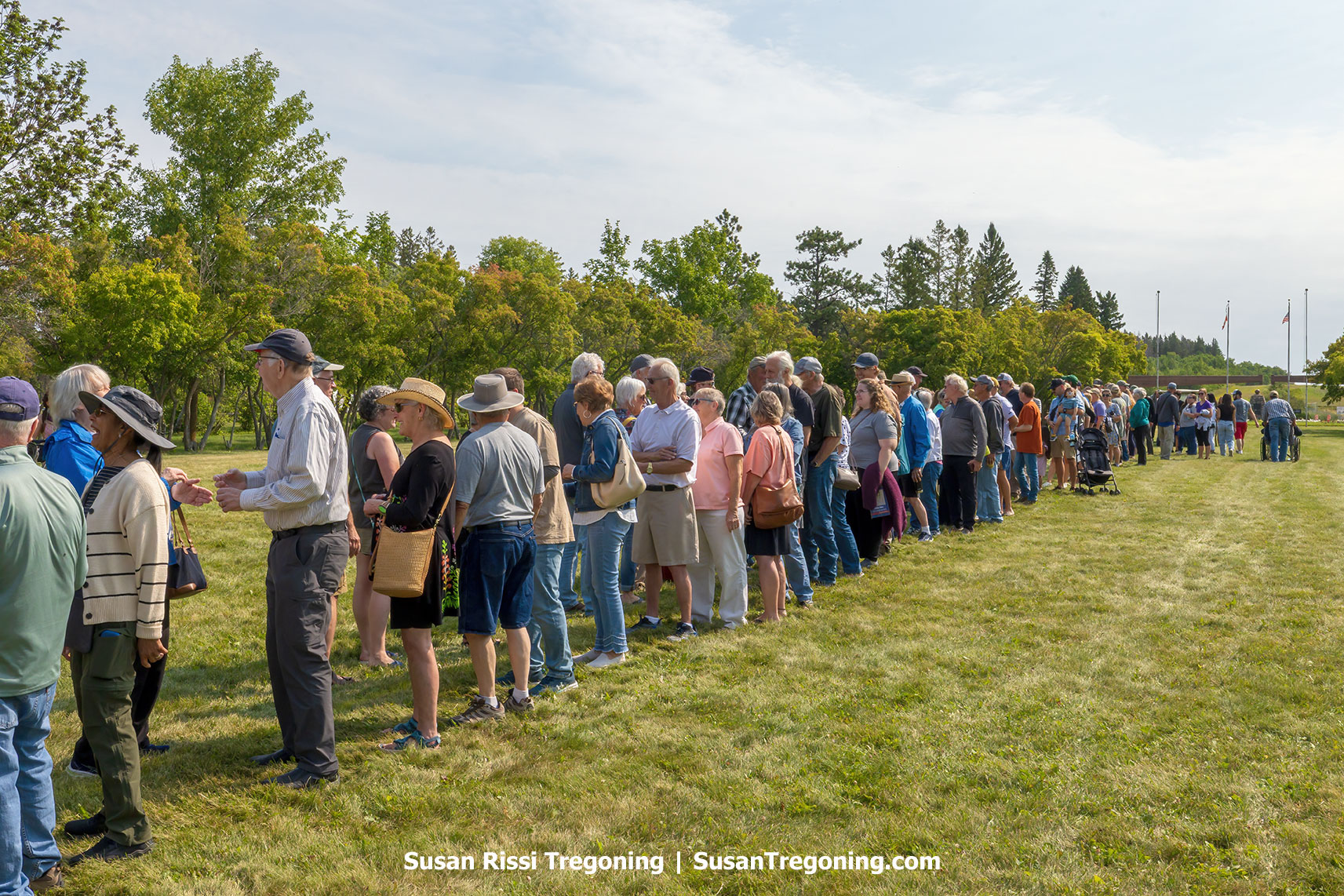 Visitors from the United States and Canada gather in a long line on the grassy border at the International Peace Garden, reaching out to shake hands during the annual Handshake Across the Border event.