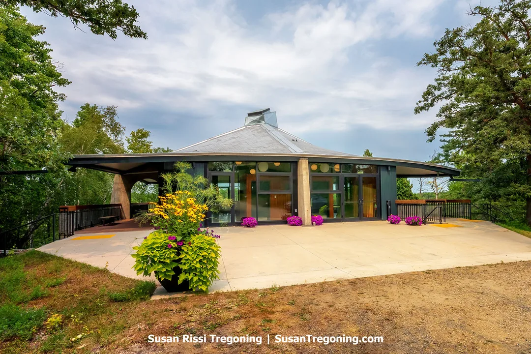 Willis Pavilion at the International Peace Garden, a 1967 modernist structure built for Canada’s Centennial, surrounded by tall trees, colorful flowerbeds, and soft natural light.